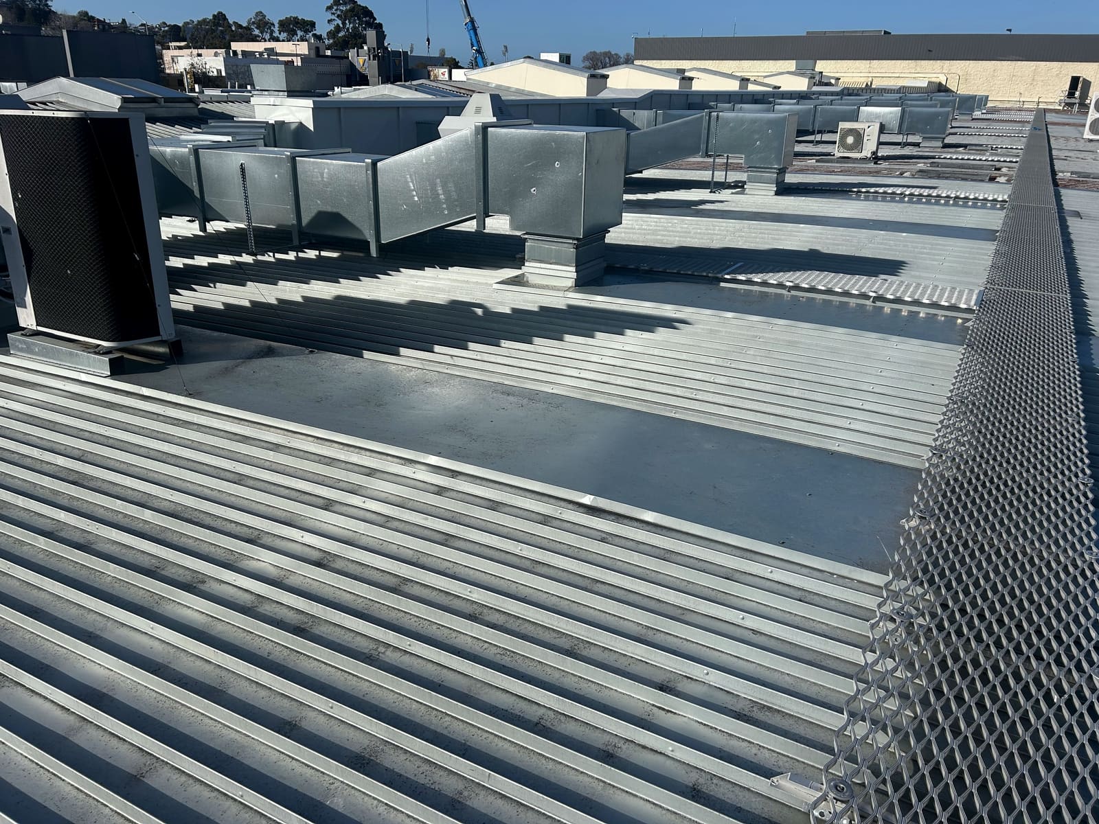 An existing commercial metal roof with large ducting runs, condenser units and walkway mesh.