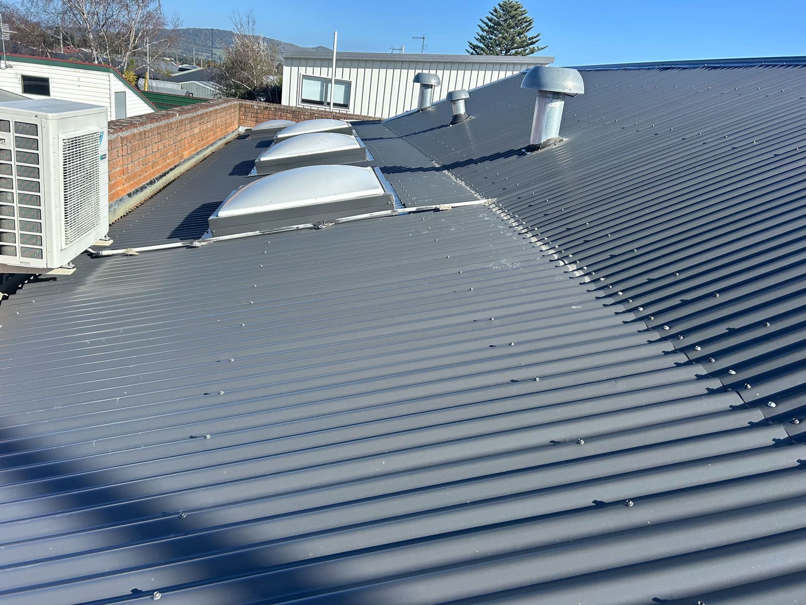 New charcoal corrugated roof with domed skylights and two cowl vents, alongside a brick parapet.