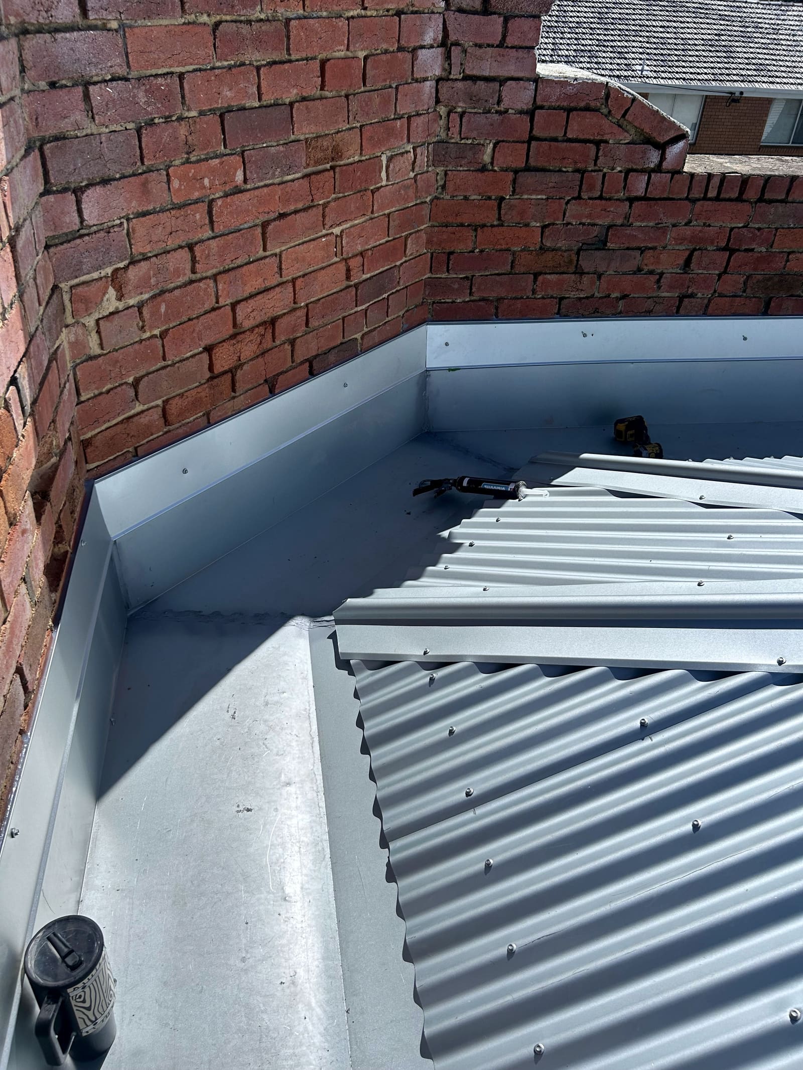 New box gutter and valley flashing in a brick corner, with new corrugated sheeting being laid over it.
