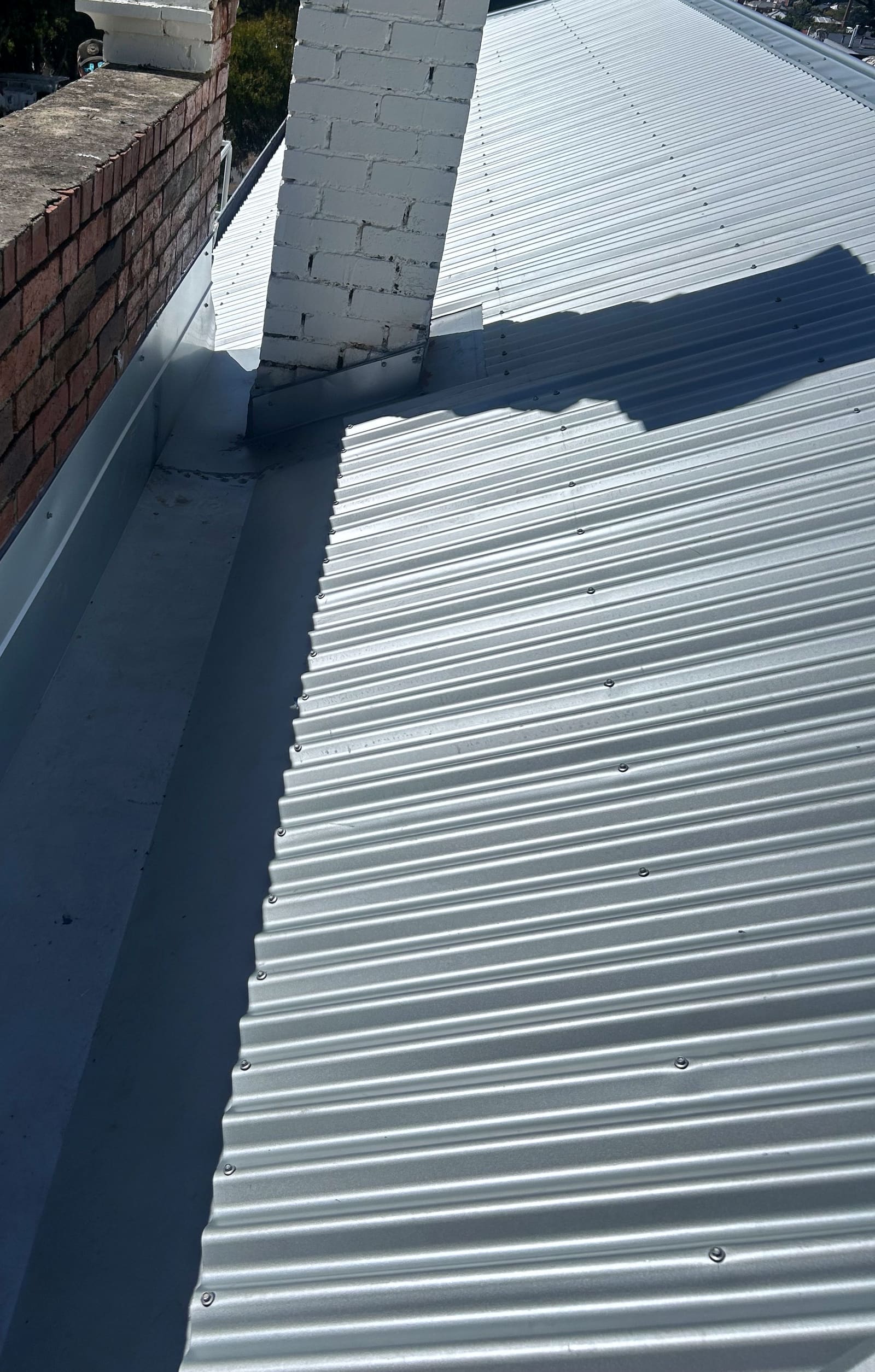 New corrugated sheeting and flashing finished against a rendered chimney and a brick parapet wall.